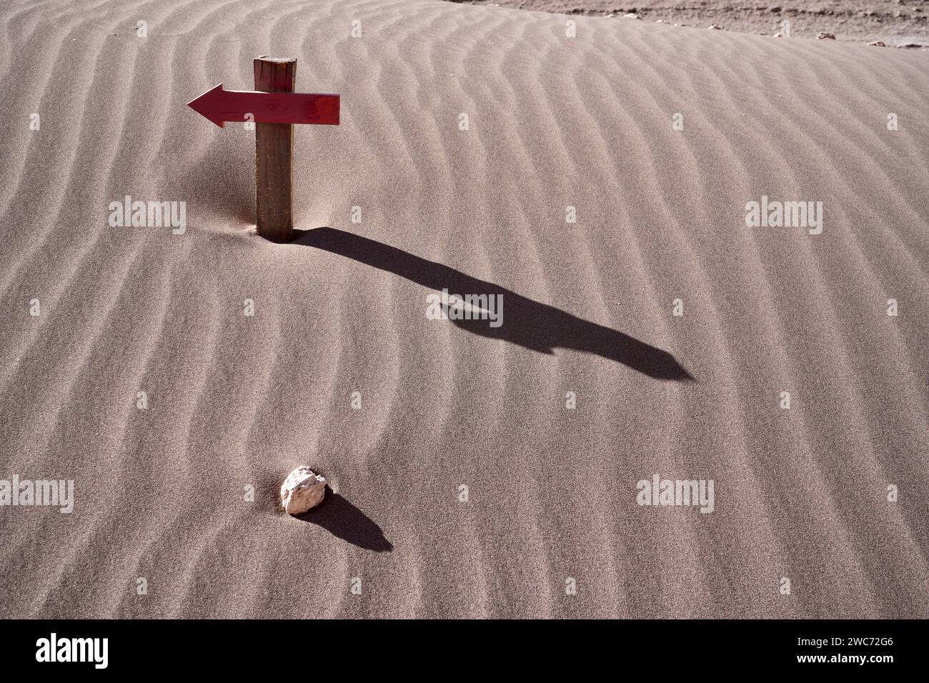 Croce a freccia in legno con ombra e roccia isolata su una duna di sabbia. San Pedro de Atacama, Cile. Foto Stock