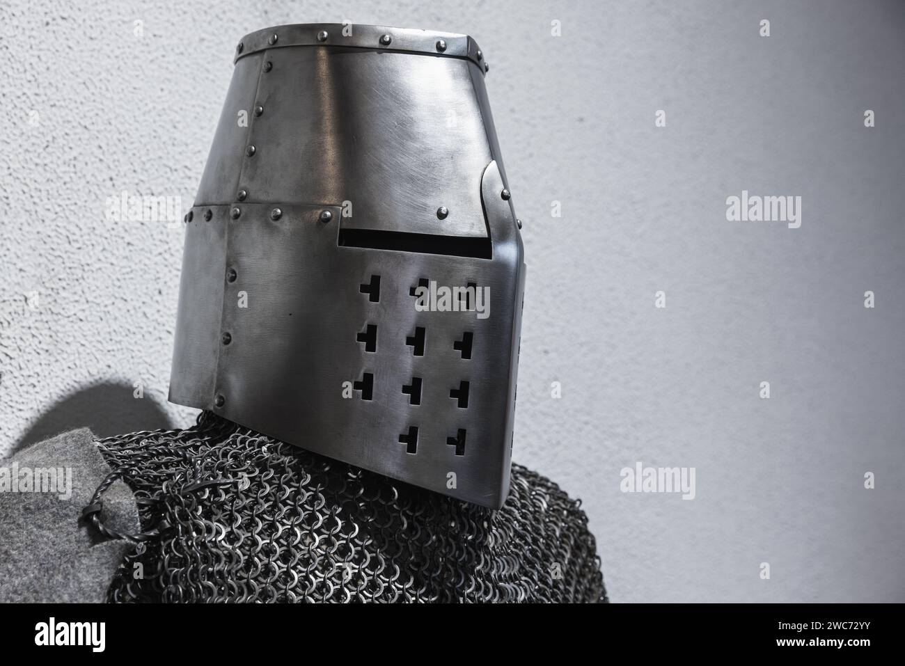 Armatura in acciaio di un cavaliere crociato medievale. Casco in ferro chiuso e catena su parete grigia Foto Stock