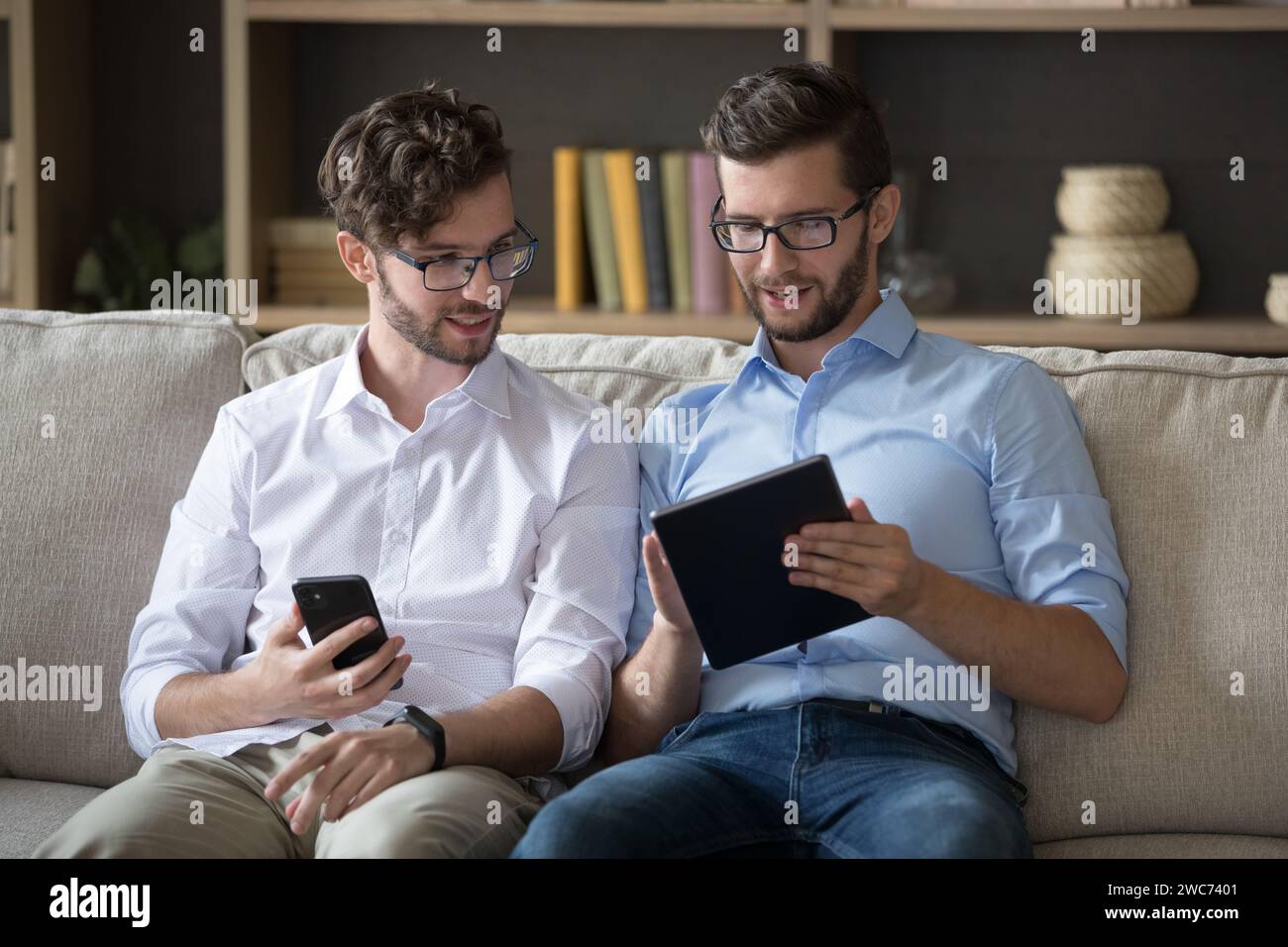 Due fratelli gemelli seduti sul divano con i dispositivi Foto Stock