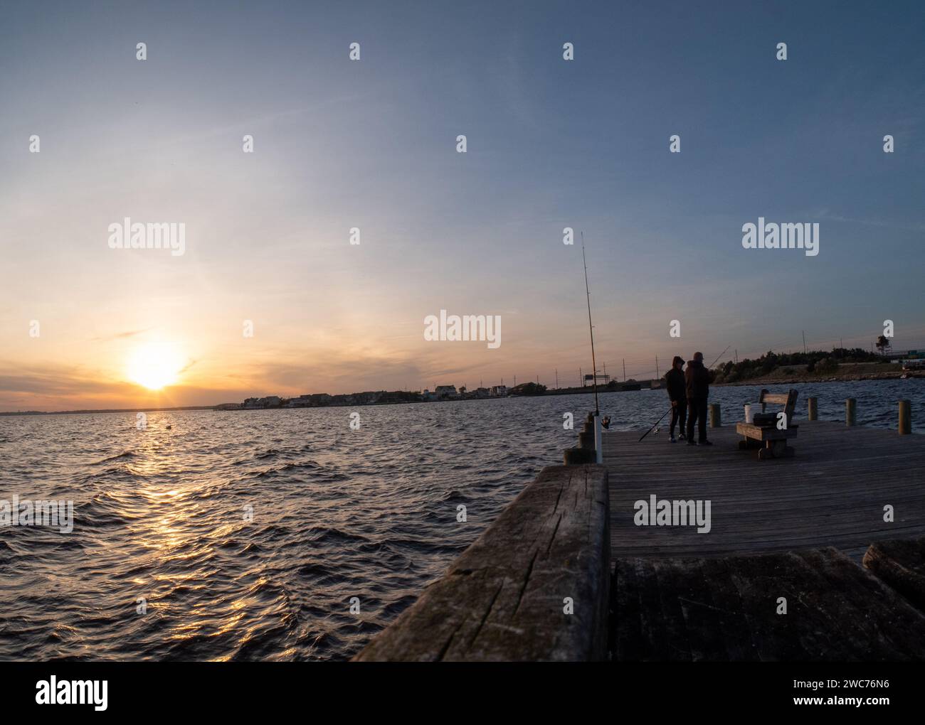 Un gruppo di individui si impegna nella serena attività di pesca al largo di un pittoresco molo durante l'ora d'oro del tramonto in un'incantevole cittadina sull'isola Foto Stock