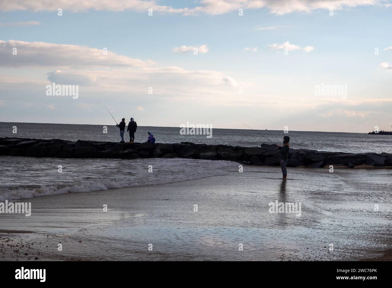 Due persone si godono una serena serata in spiaggia, impegnandosi nella rilassante attività di pesca mentre si crogiolano al caldo bagliore del sole che tramonta Foto Stock