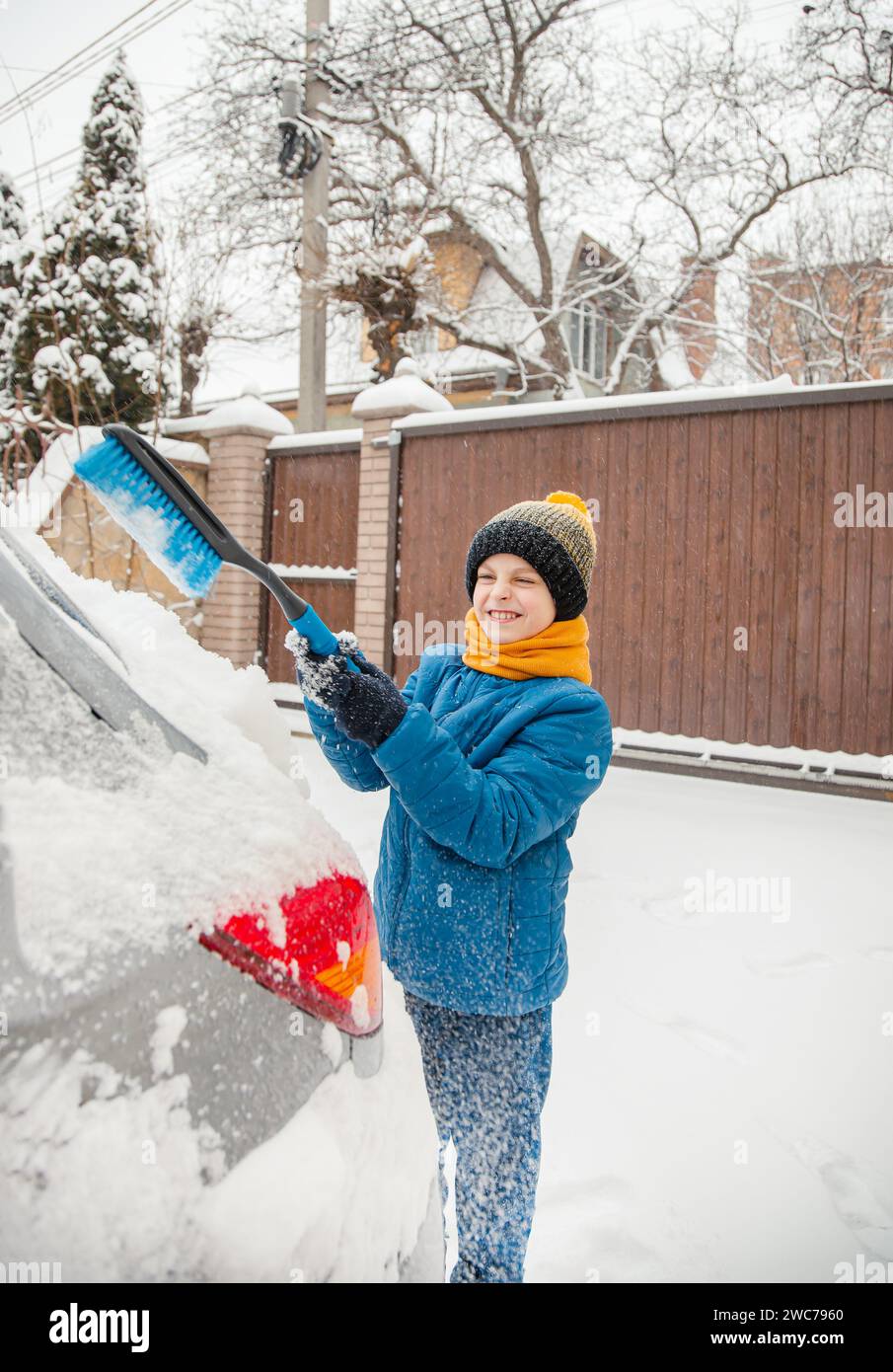 Il bambino carino sta aiutando suo padre a spazzolare la neve dalla macchina. Rimozione della neve dalla vettura - il concetto di cura della vettura durante l'inverno. Foto Stock