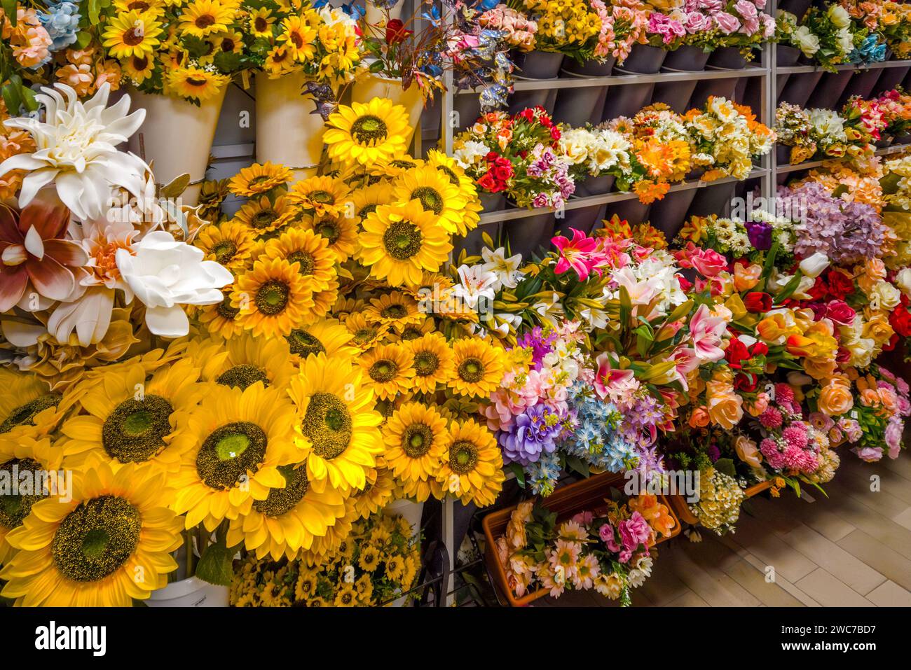 Falsi fiori mutlicolori, girasoli e altri tipi di fiori artificiali esposti sullo scaffale del fiorista Foto Stock