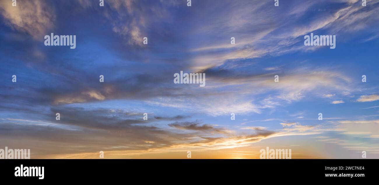Il sole tramonta una sinfonia di luce e nuvole, che proietta un sereno bagliore sul cielo serale. Foto Stock