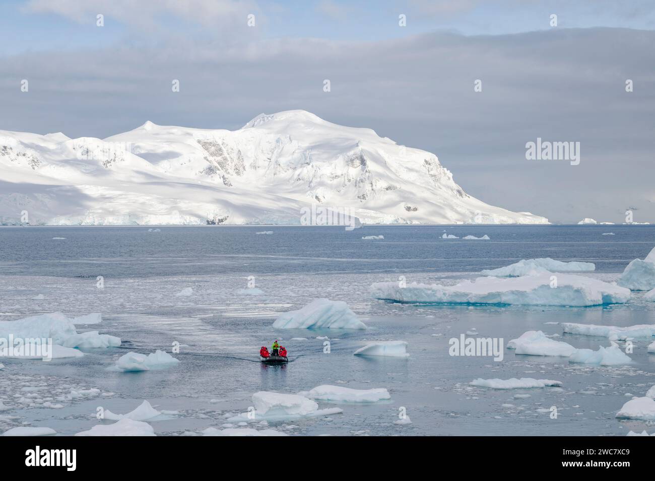 Zodiaco che naviga attraverso il ghiaccio al porto di Neko, in Antartide, acqua piena di ghiaccio e iceberg ancorati al suo posto, riflessi e picchi innevati Foto Stock