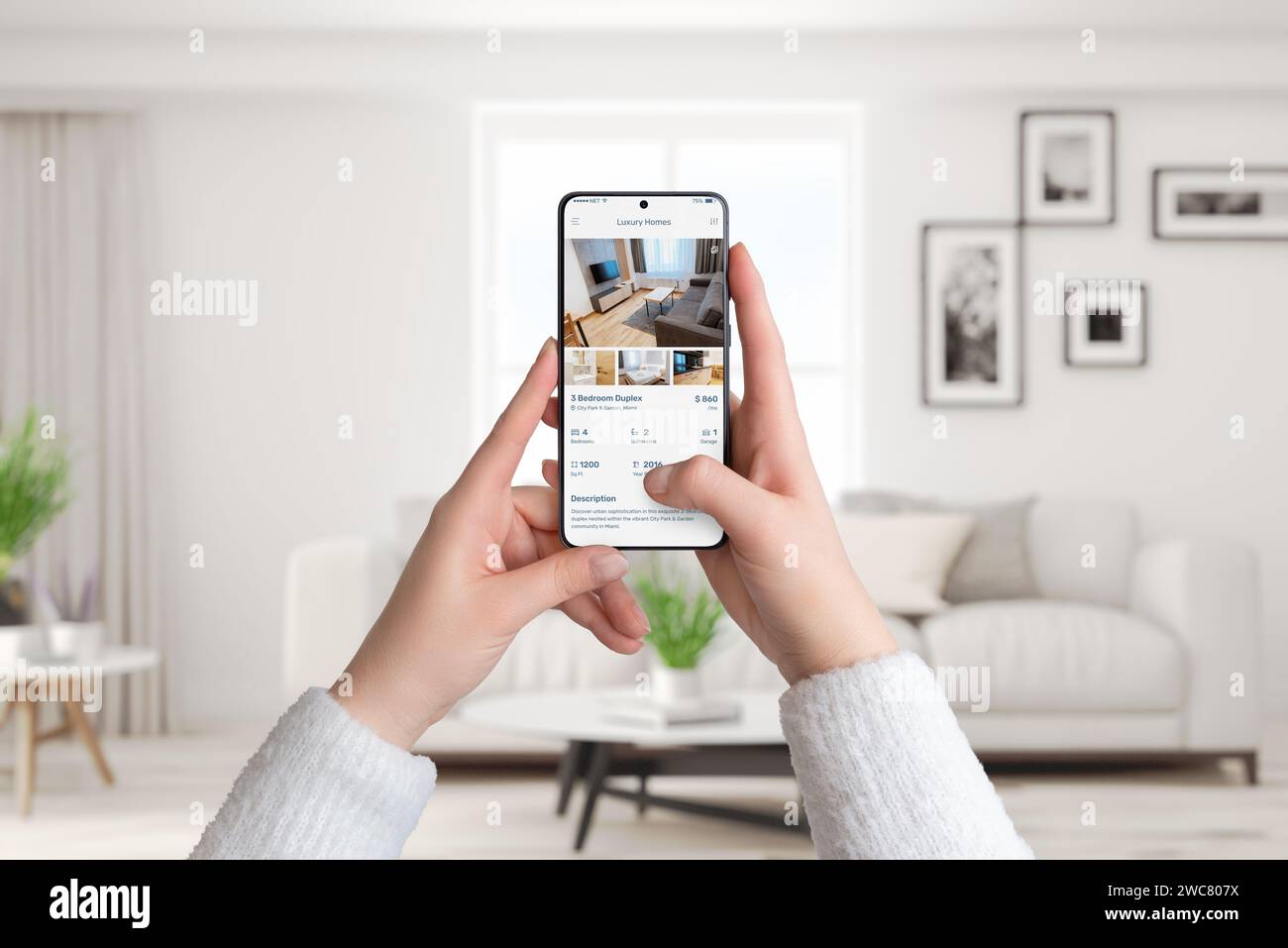 Le mani di una donna tengono uno smartphone all'interno di un salotto. Utilizzo di un'app per case di lusso per cercare l'affitto, combinando tecnologia moderna e sofisticata Foto Stock
