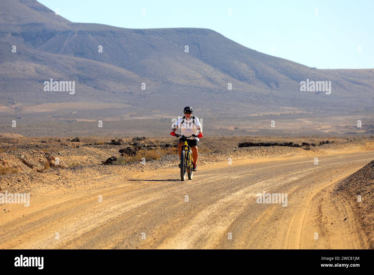 Un uomo in bicicletta su un sentiero polveroso, El Cotillo, Fuerteventura, novembre 2023. Foto Stock