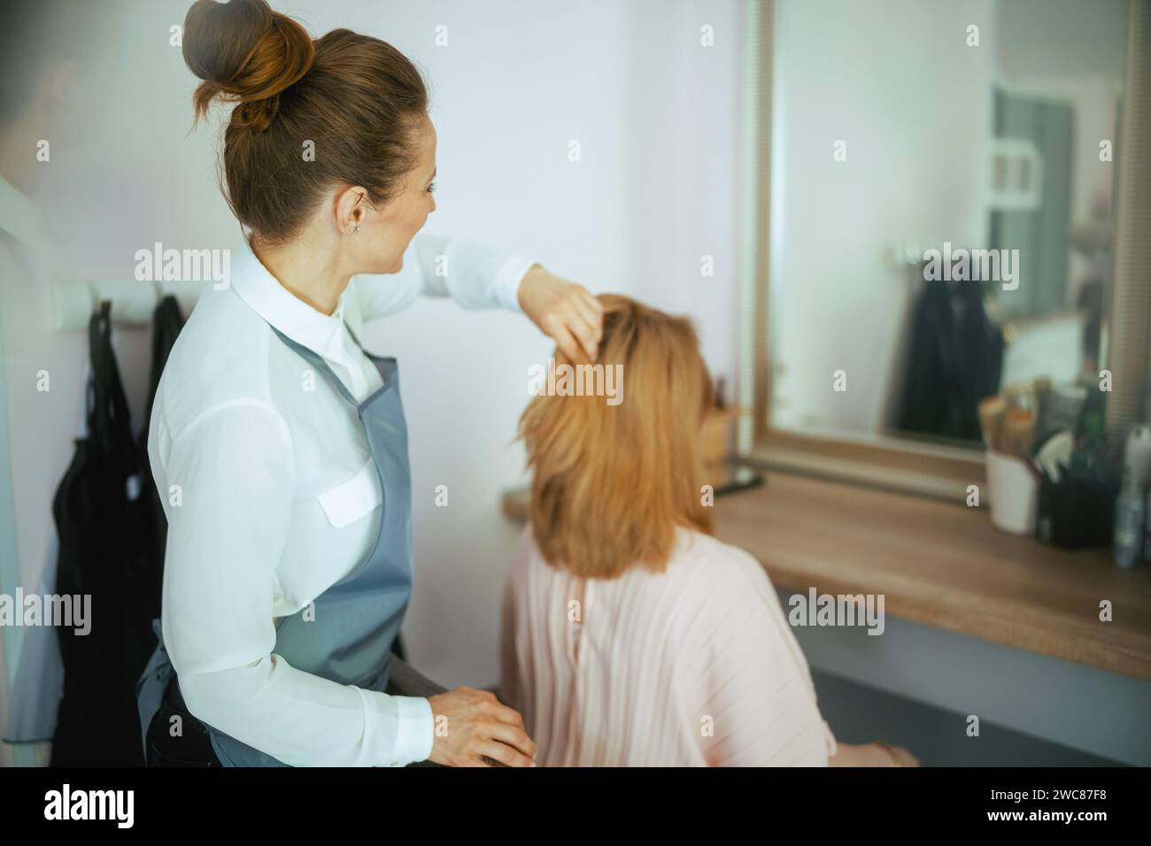 Vista da dietro parrucchiere donna in un moderno studio di parrucchiere con cliente. Foto Stock