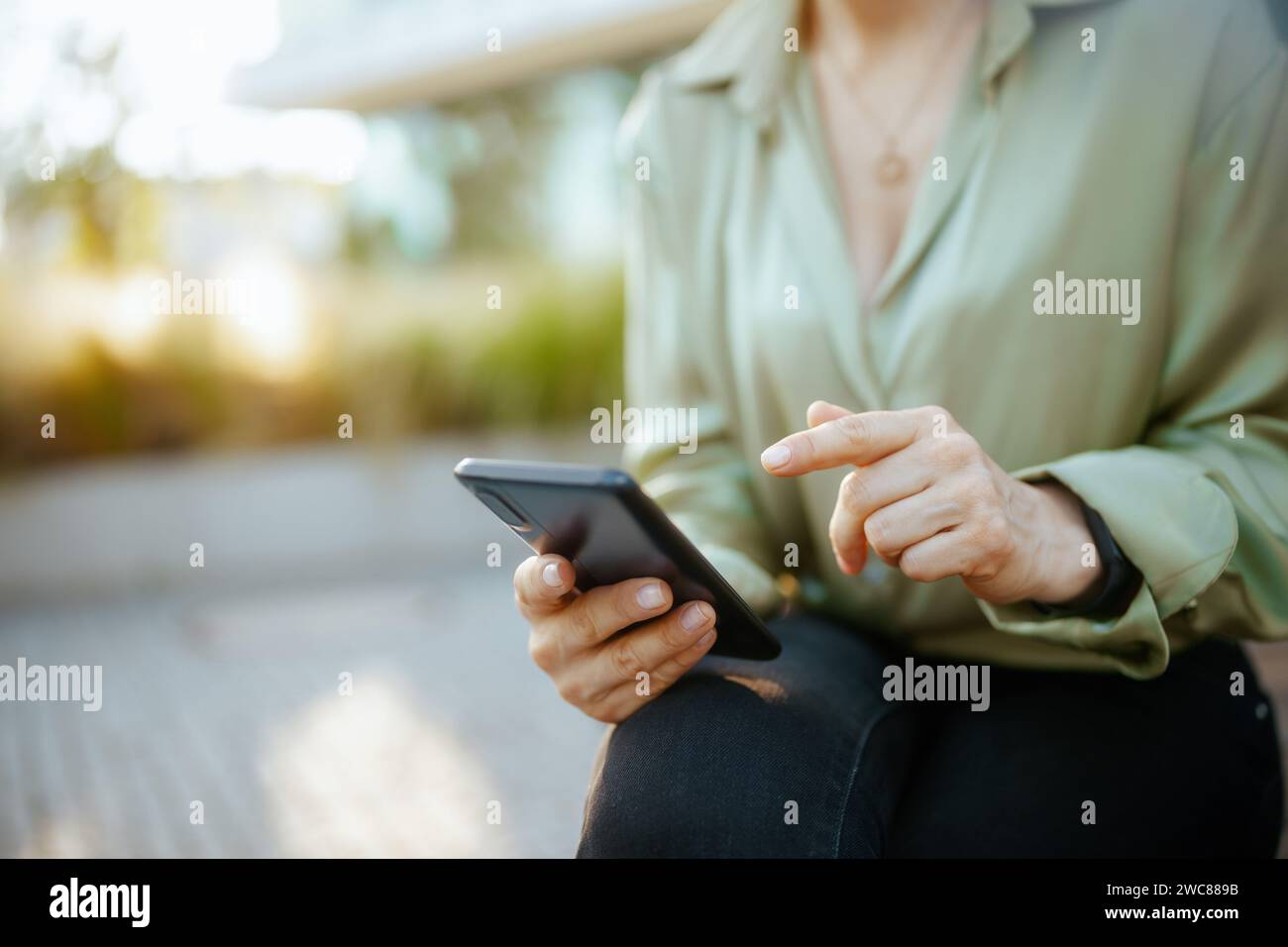 Primo piano su una donna d'affari nel quartiere degli affari in camicetta verde e occhiali da vista con smartphone. Foto Stock