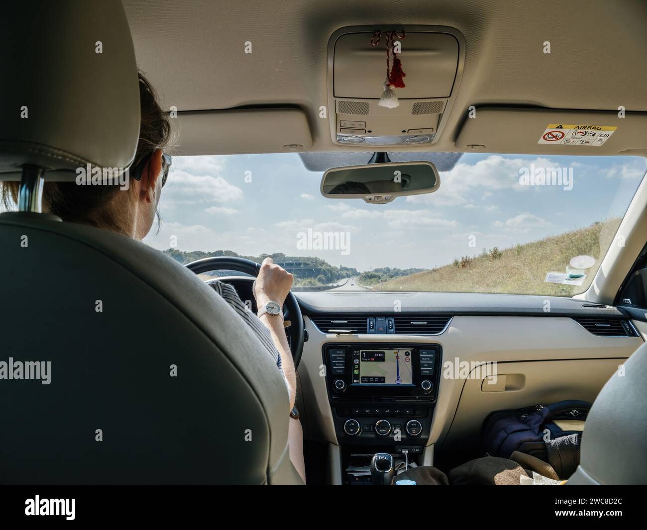 Francia - 17 agosto 2023: Un autista donna all'interno di un'auto che guarda la strada prospettica verso la destinazione utilizzando Apple CarPlay e Apple Maps per spostarsi, catturando la quintessenza di un viaggio su strada lungo un pittoresco percorso illuminato dal sole. Foto Stock