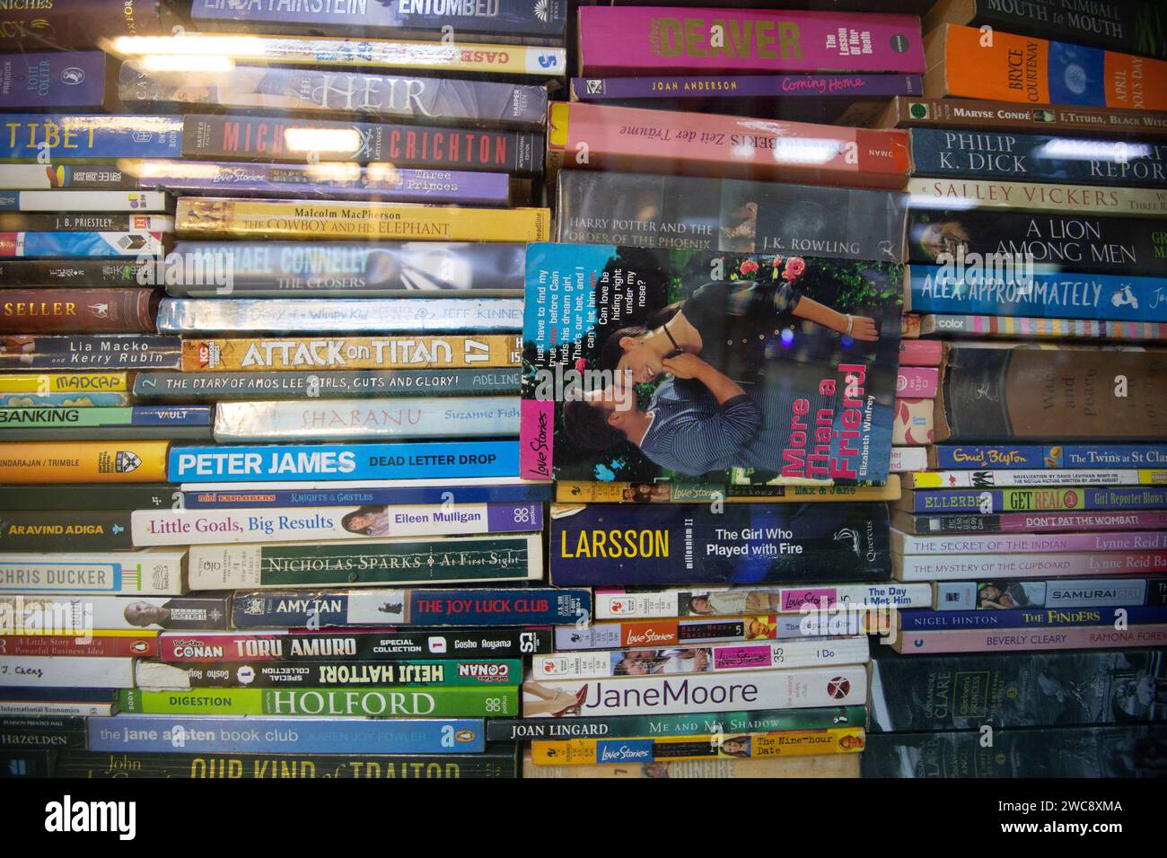 Una pila di libri usati con rilegatura morbida e rigida impilati su una finestra trasparente esposta all'interno di una libreria di seconda mano. Foto Stock