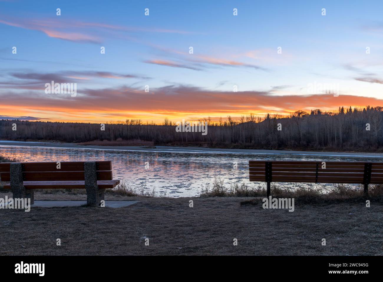 Parco della città di Edmonton Fort Edmonton Footbridge con due panchine di fronte al tramonto del fiume nella tarda stagione autunnale e ghiaccio Foto Stock