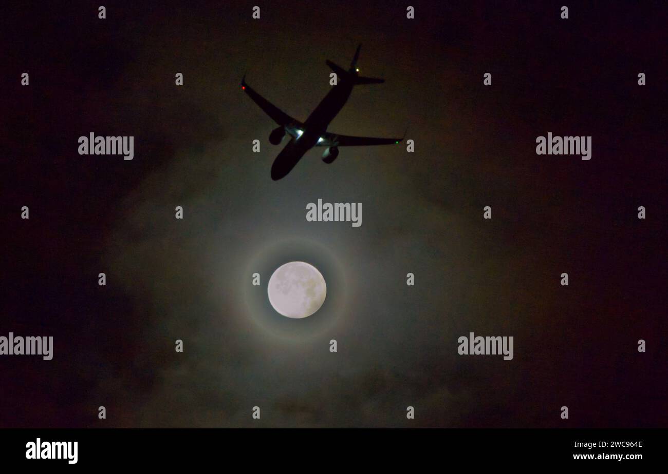 Un aereo in volo notturno vicino all'alone della luna piena (esposizione in stile retrò) Foto Stock
