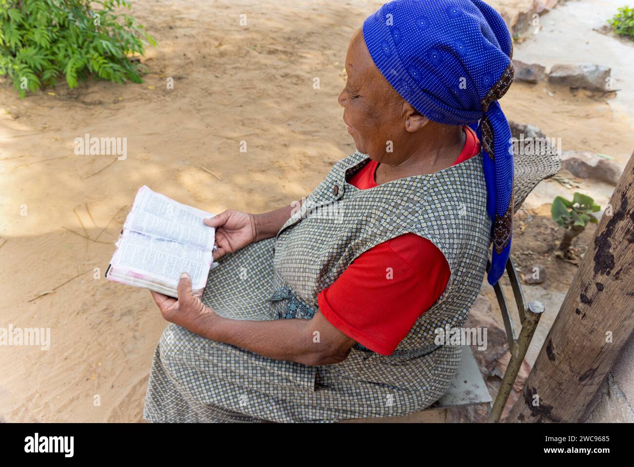 Vecchia donna africana che legge la bibbia nel cortile, villaggio in Botswana Foto Stock