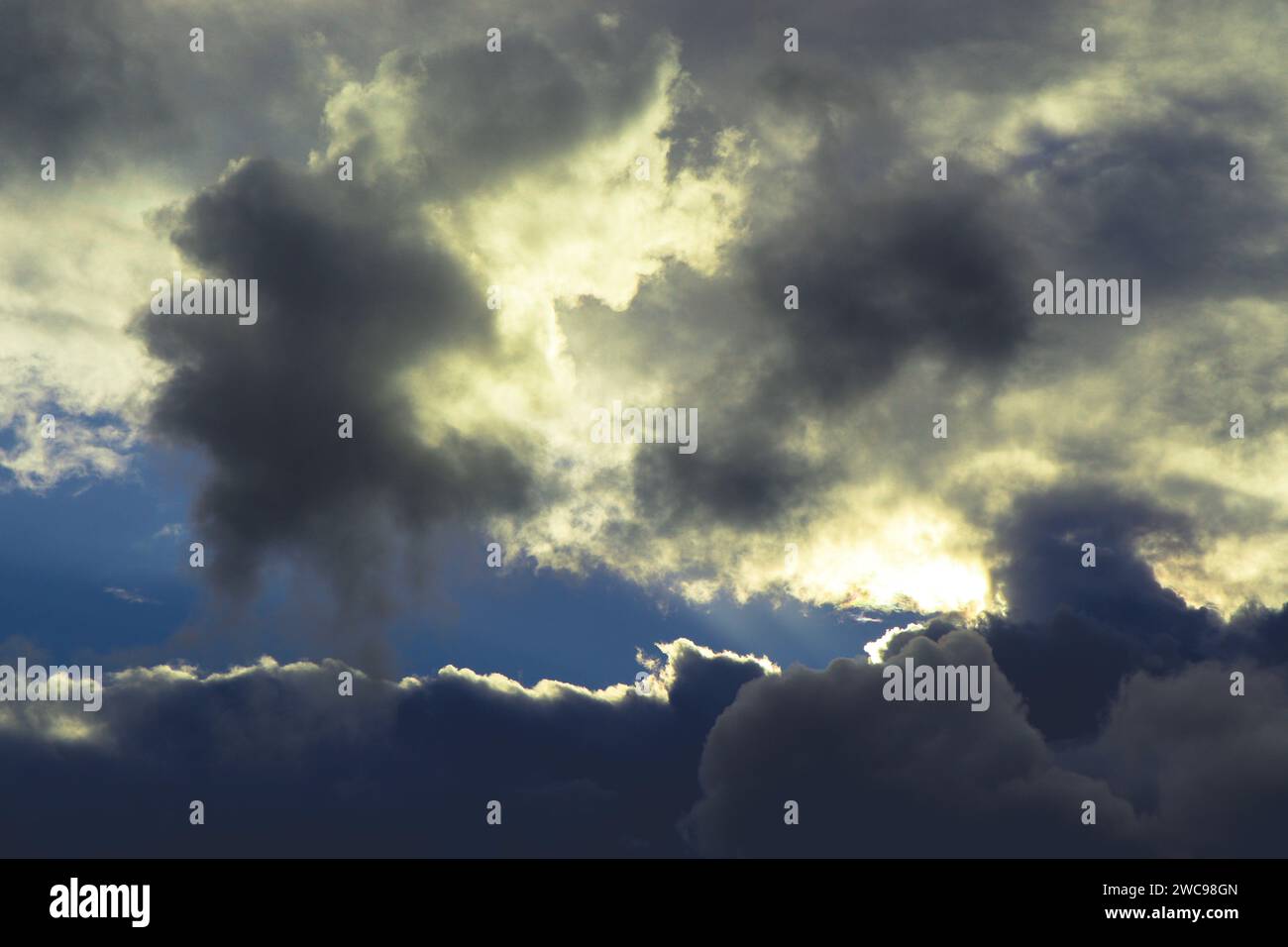 Nuvole invernali bianche e grigie con sfondo blu. Il sole cerca di sfondare le nuvole come un occhio nel cielo. Foto Stock