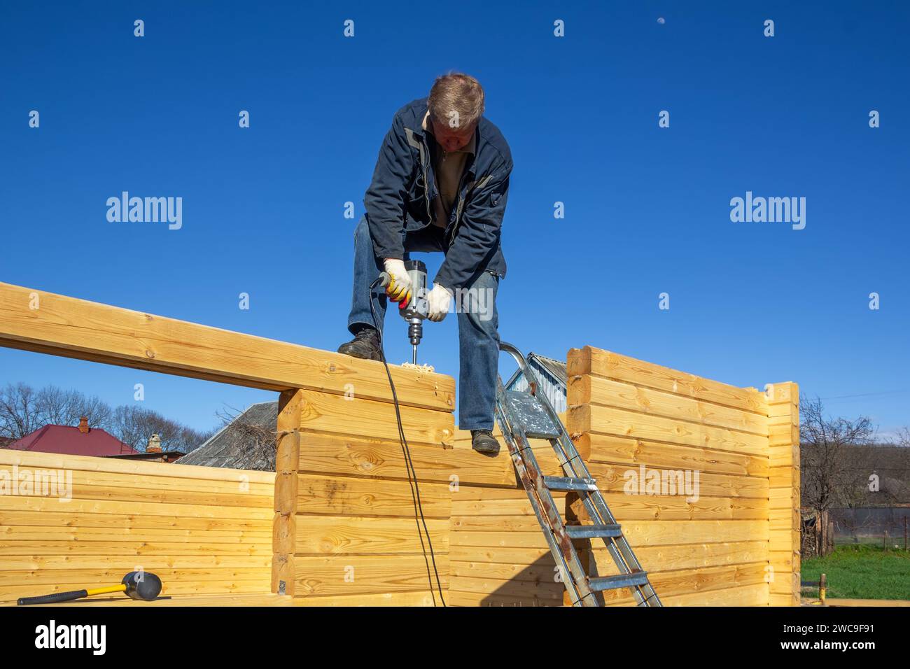 un uomo costruisce una casa di legno fatta di legno profilato in campagna contro il cielo blu Foto Stock
