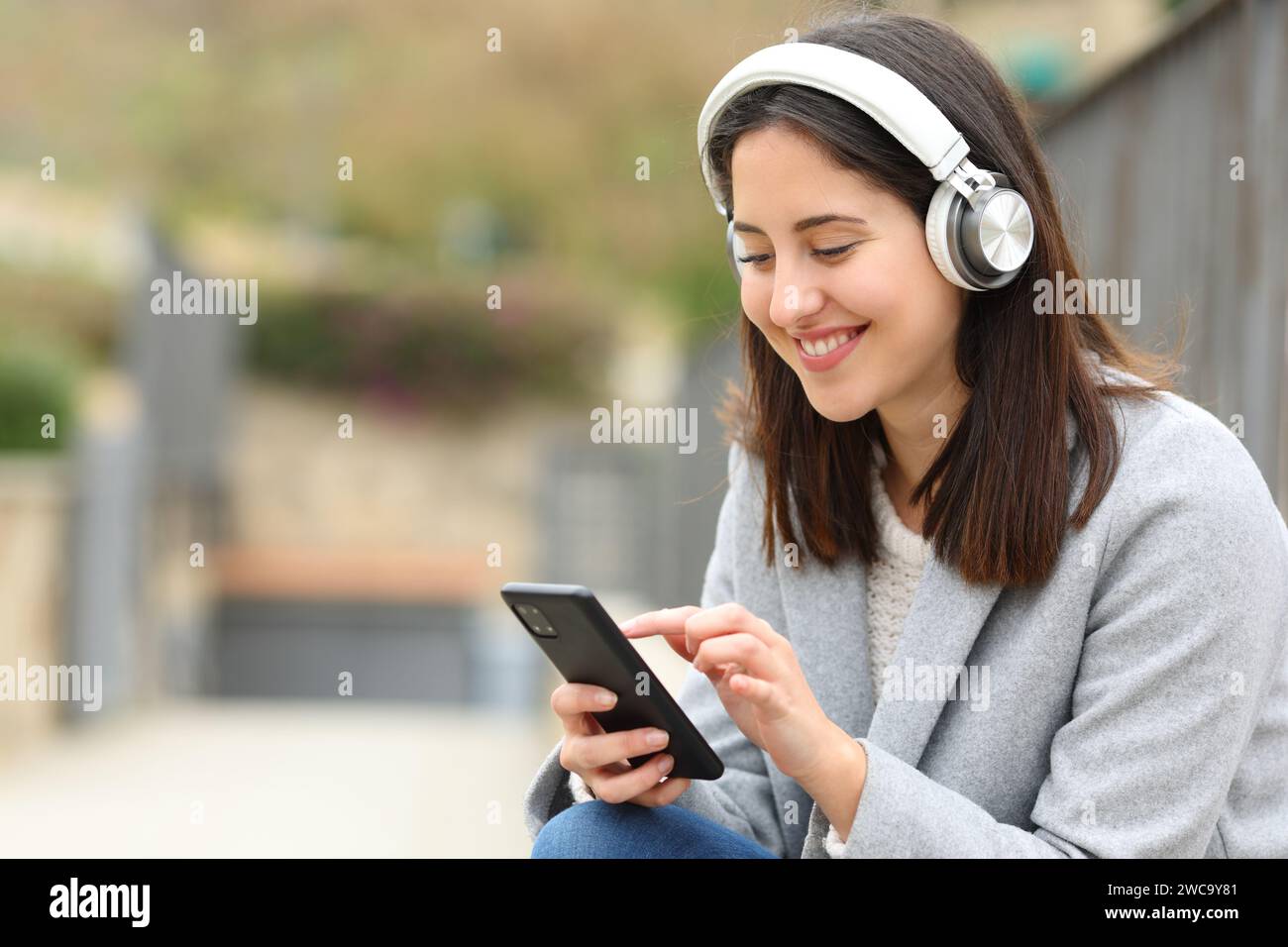 Donna seduta per strada che usa il telefono per ascoltare musica Foto Stock