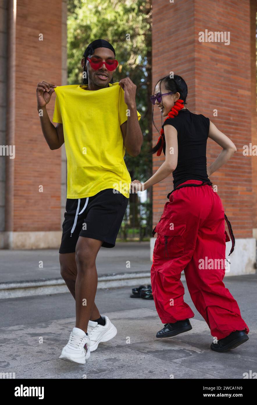 Una serie di immagini che catturano l'energia allegra di due compagni di danza in uno streetwear vivace, condividendo una danza e un caldo abbraccio sul marciapiede. Foto Stock