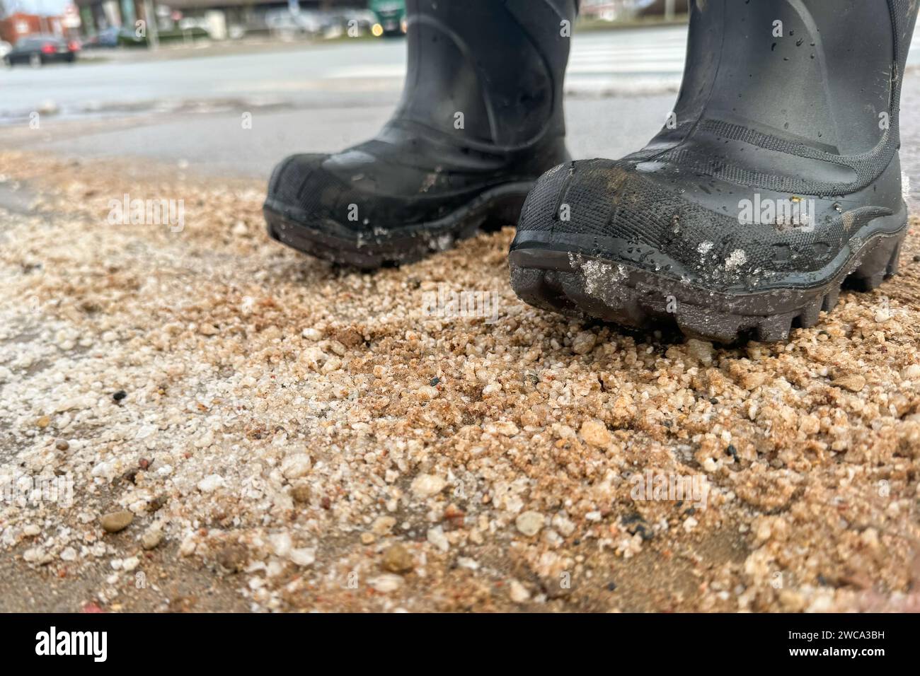 Stare in piedi con gli stivali su una strada sporca, sale e sabbia sulla strada in inverno. Foto Stock