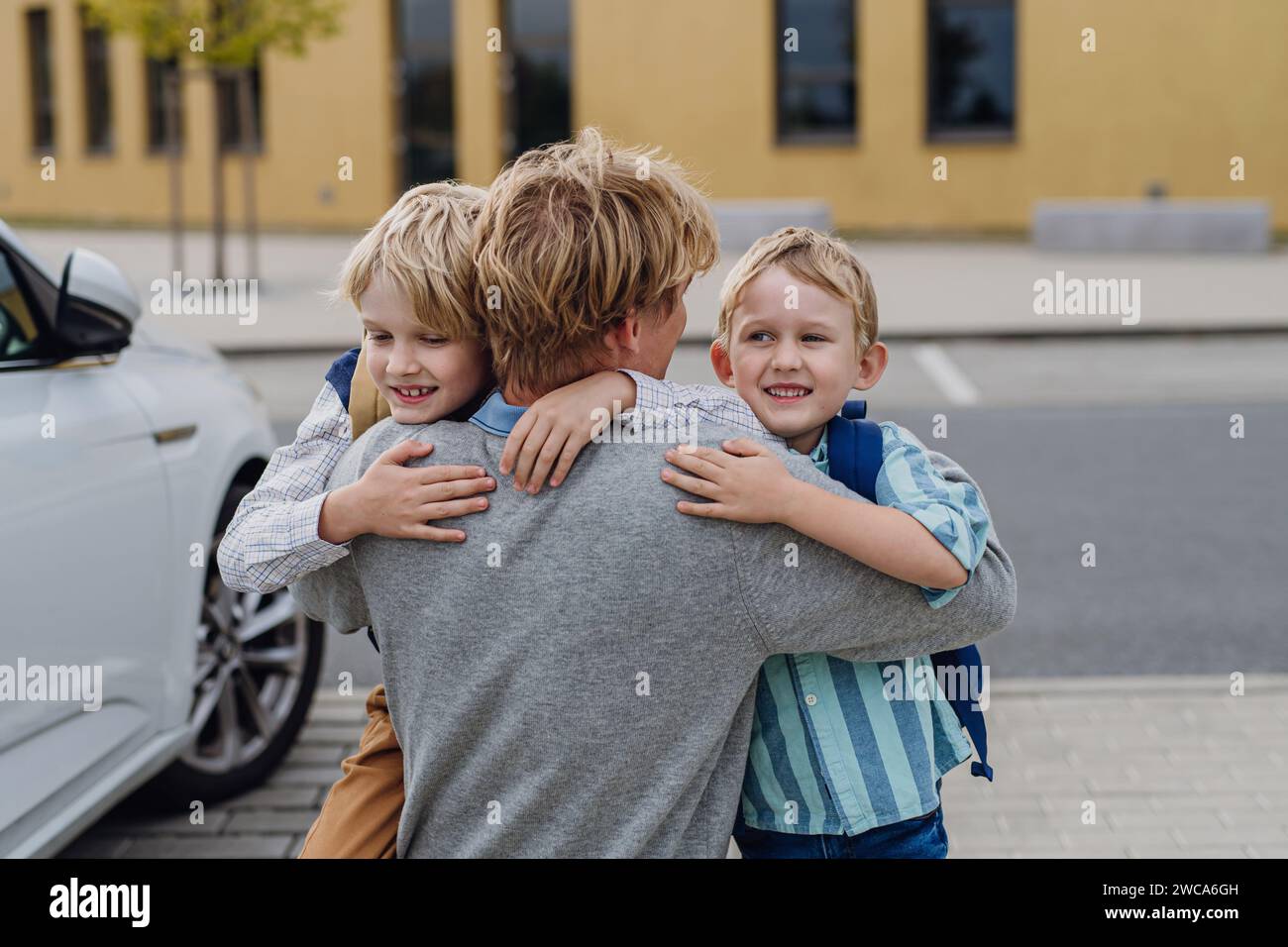 Padre che salutava i figli di fronte all'edificio scolastico, li abbracciava. Papa' va al lavoro. Concetto di equilibrio vita-lavoro per i genitori. Foto Stock