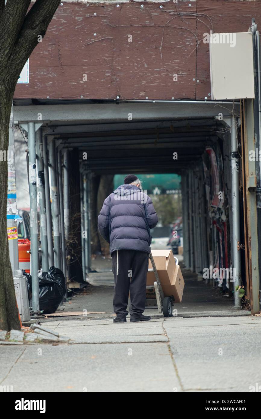 Un anonimo operaio ebreo ortodosso spinge un camion a mano davanti a un cantiere in Ross St a Williamsburg, Brooklyn, il giorno di Natale Foto Stock