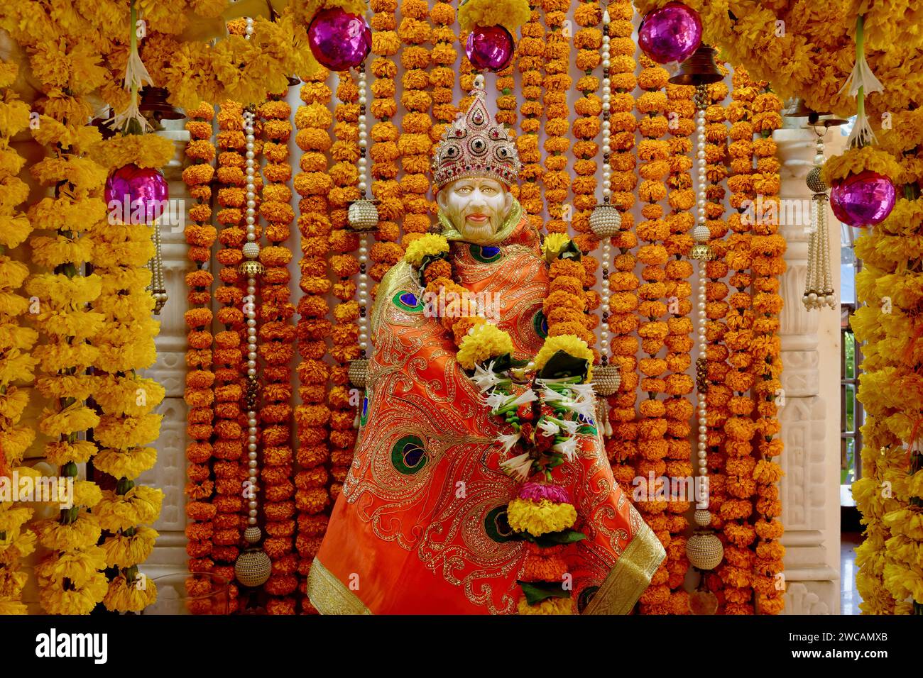 Un santuario di preghiera con una statua di san Shirdi Sai Baba indù, sullo sfondo di ghirlande di fiori di calendula gialli e arancioni; Mumbai, India Foto Stock