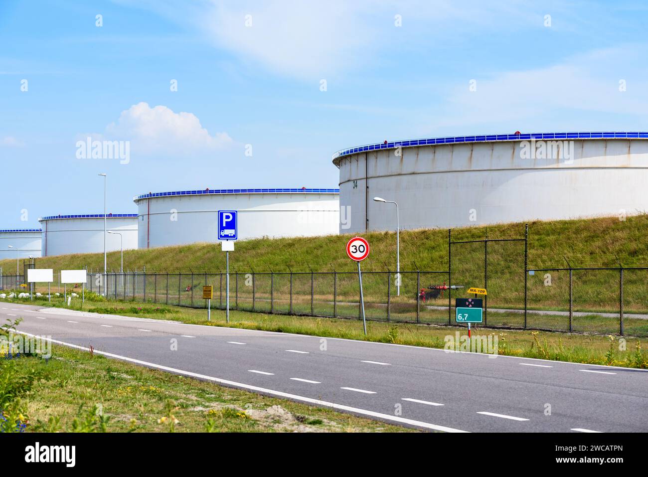 Terminal del petrolio recintato con grandi serbatoi per lo stoccaggio del petrolio greggio in un porto nelle soleggiate giornate estive Foto Stock