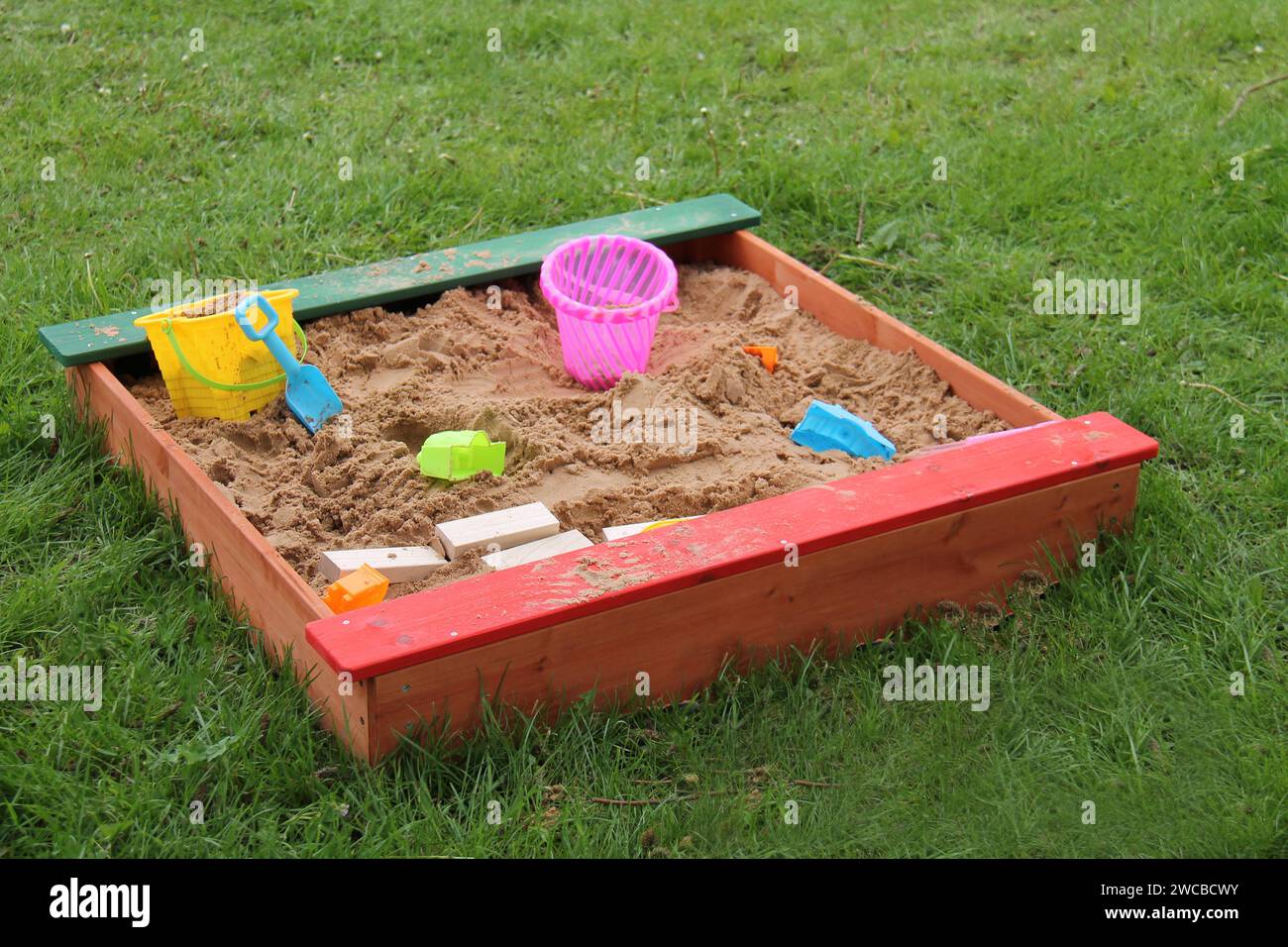 Un pozzo di sabbia in legno con alcuni giocattoli in plastica e legno. Foto Stock