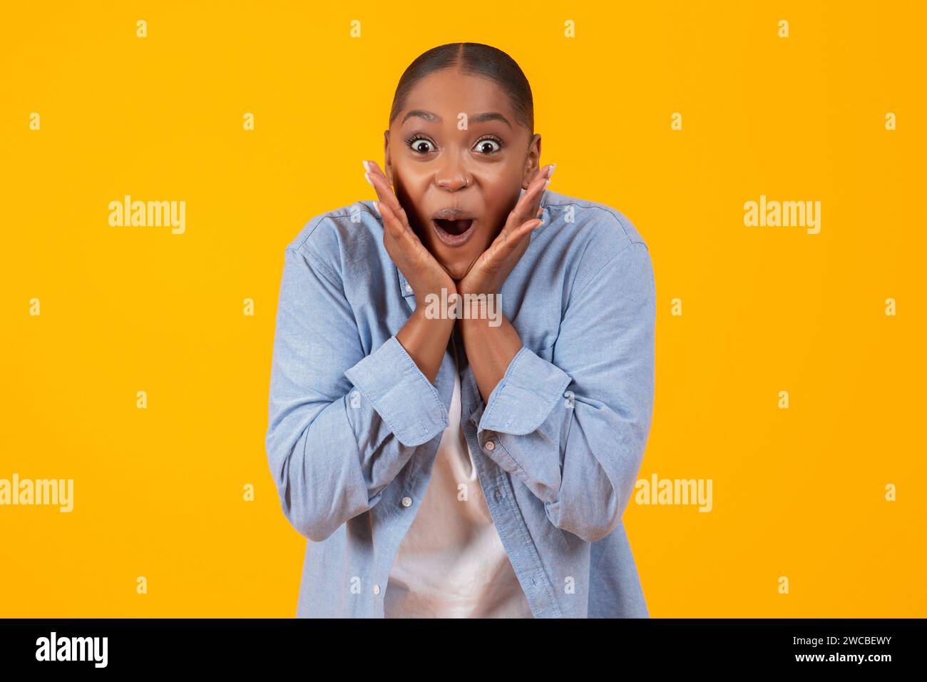 signora nera che urla eccitante toccando il volto su sfondo giallo Foto Stock