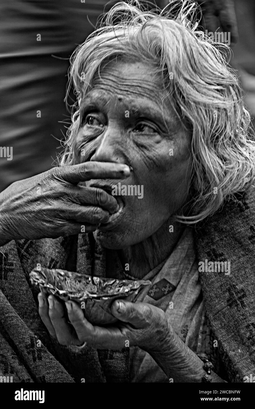 Una vecchia povera e indifesa donna indiana che mangia del cibo con un aspetto affamato e sembra molto triste Foto Stock