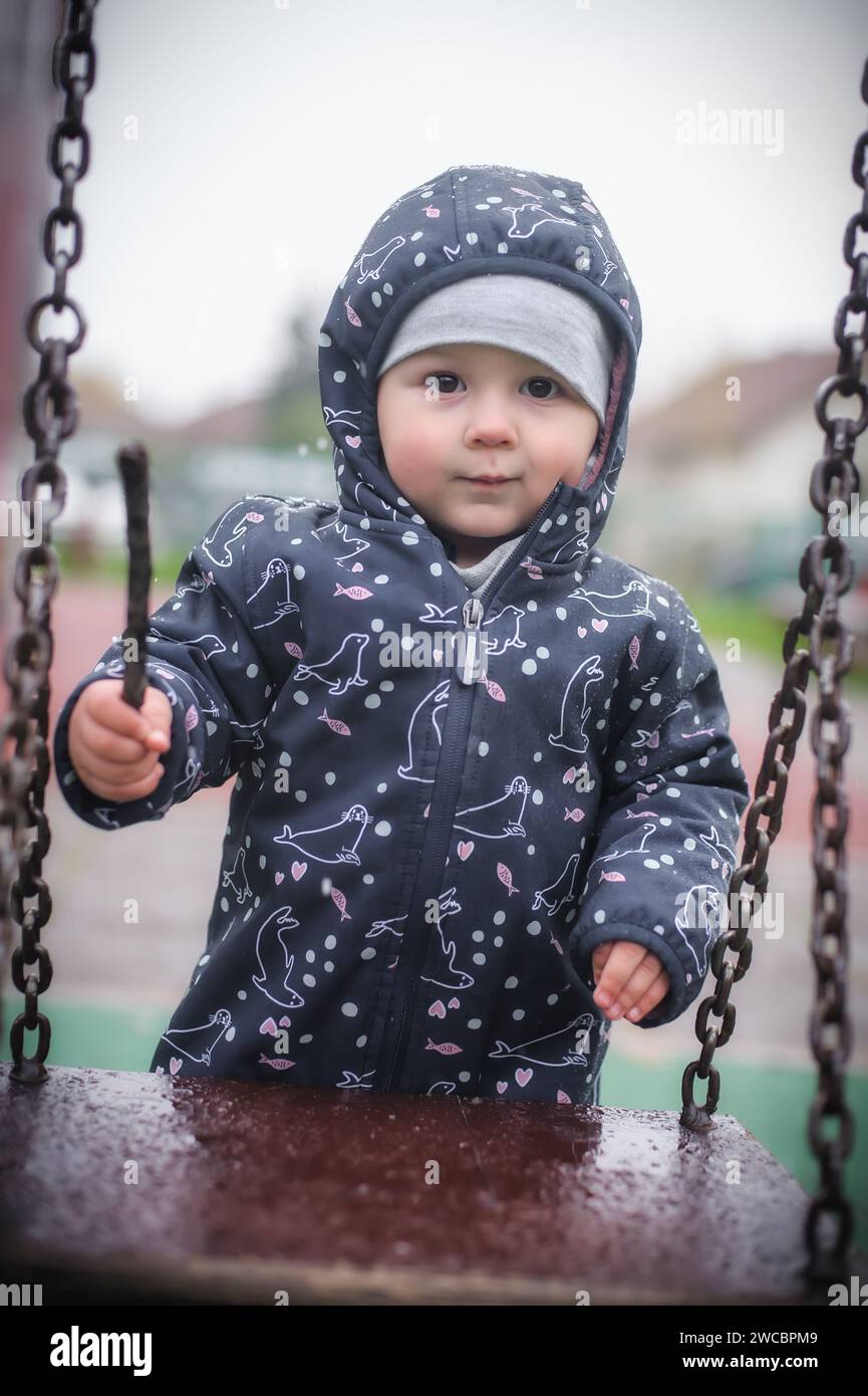 Il bambino si trova vicino a un'altalena sul parco giochi. Giochi all'aperto attivi. Felice infanzia. Intrattenimento per bambini Foto Stock