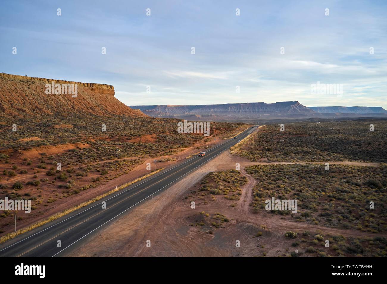 Diversi veicoli guidano la Route 9 attraverso il deserto dello Utah. Sta diventando buio e le montagne vicine catturano gli ultimi raggi di luce mentre il sole tramonta. Foto Stock