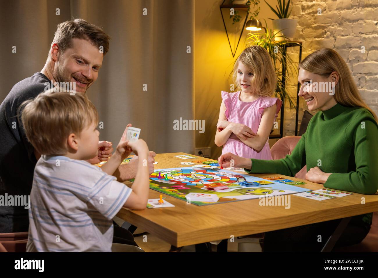 famiglia con due bambini che trascorrono il tempo insieme e giocano a giochi da tavolo seduti a casa. attività di incollaggio Foto Stock