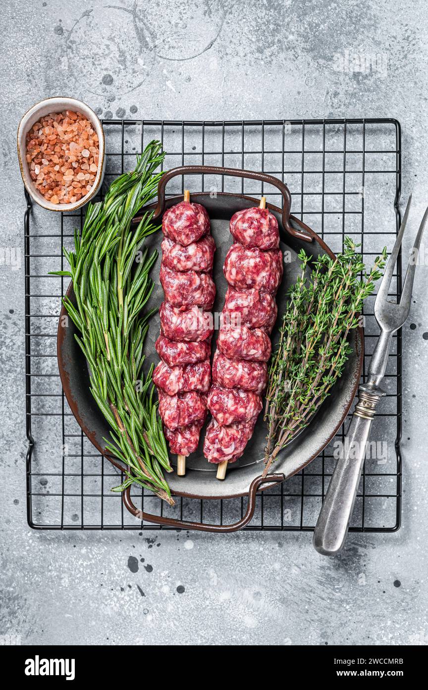 Kebab di Urfa Turco crudo decorato con erbe, spezie e forchetta di carne. Sfondo grigio. Vista dall'alto. Foto Stock