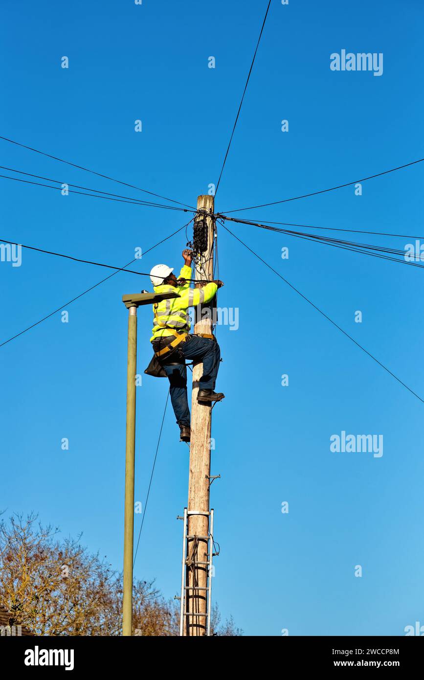 Un tecnico del telefono che fissa i cavi sulla parte superiore di un palo del telegrafo Foto Stock