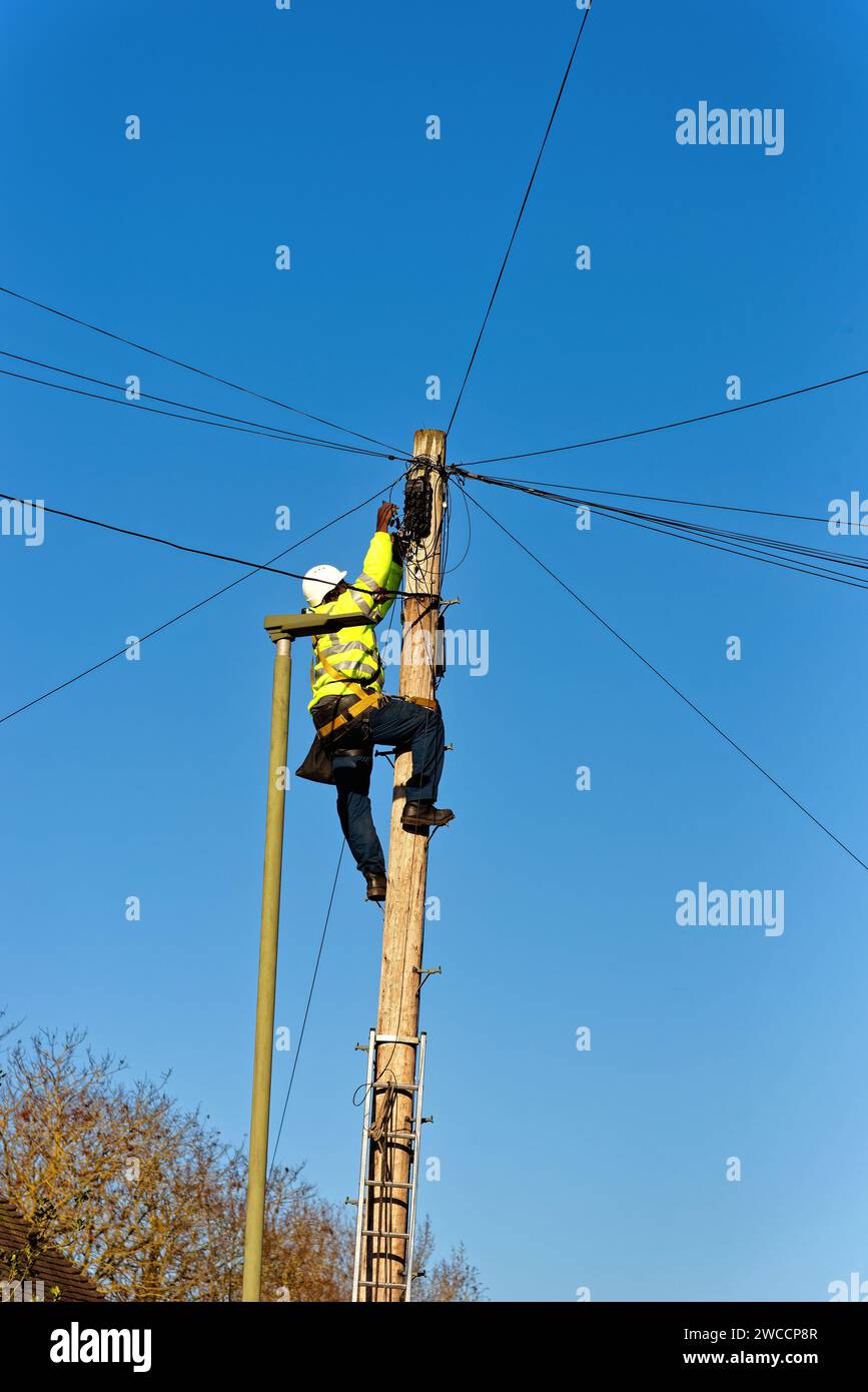 Un tecnico del telefono che fissa i cavi sulla parte superiore di un palo del telegrafo Foto Stock