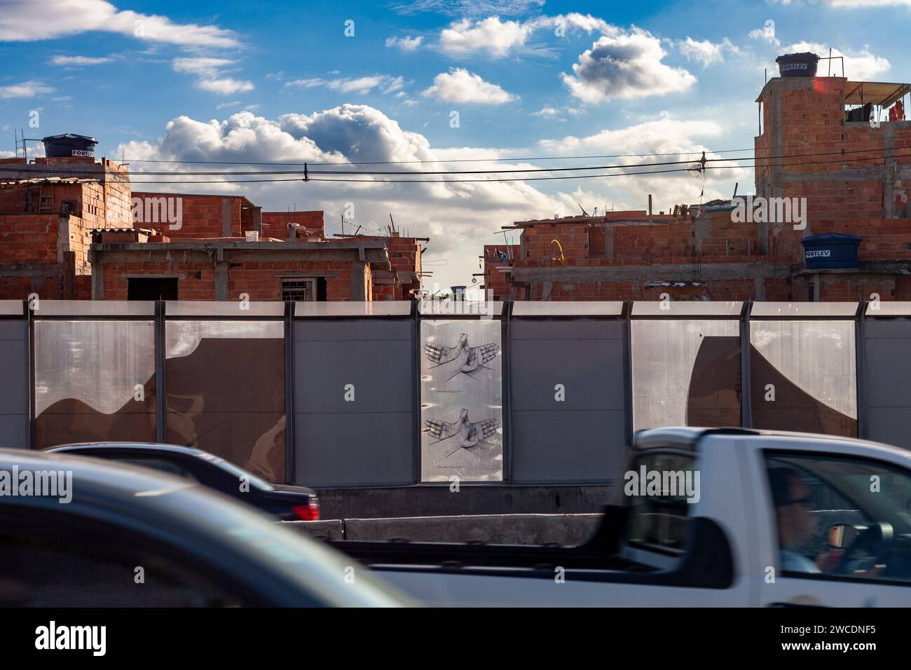 Complexo da Mare, un'enorme rete di favelas che si trova lungo la Linha Vermelha (linea rossa), l'autostrada principale che collega l'aeroporto internazionale di Rio de Janeiro al centro della città - dal 2010 la comunità è recintata dall'autostrada da enormi pannelli Perspex - una barriera di separazione lunga 7 km, alta 3 metri, decorata con graffiti - le autorità affermano che fornisce una barriera acustica, la gente del posto lo descrive come un “muro della vergogna”, un altro modo per nascondere i poveri. Foto Stock