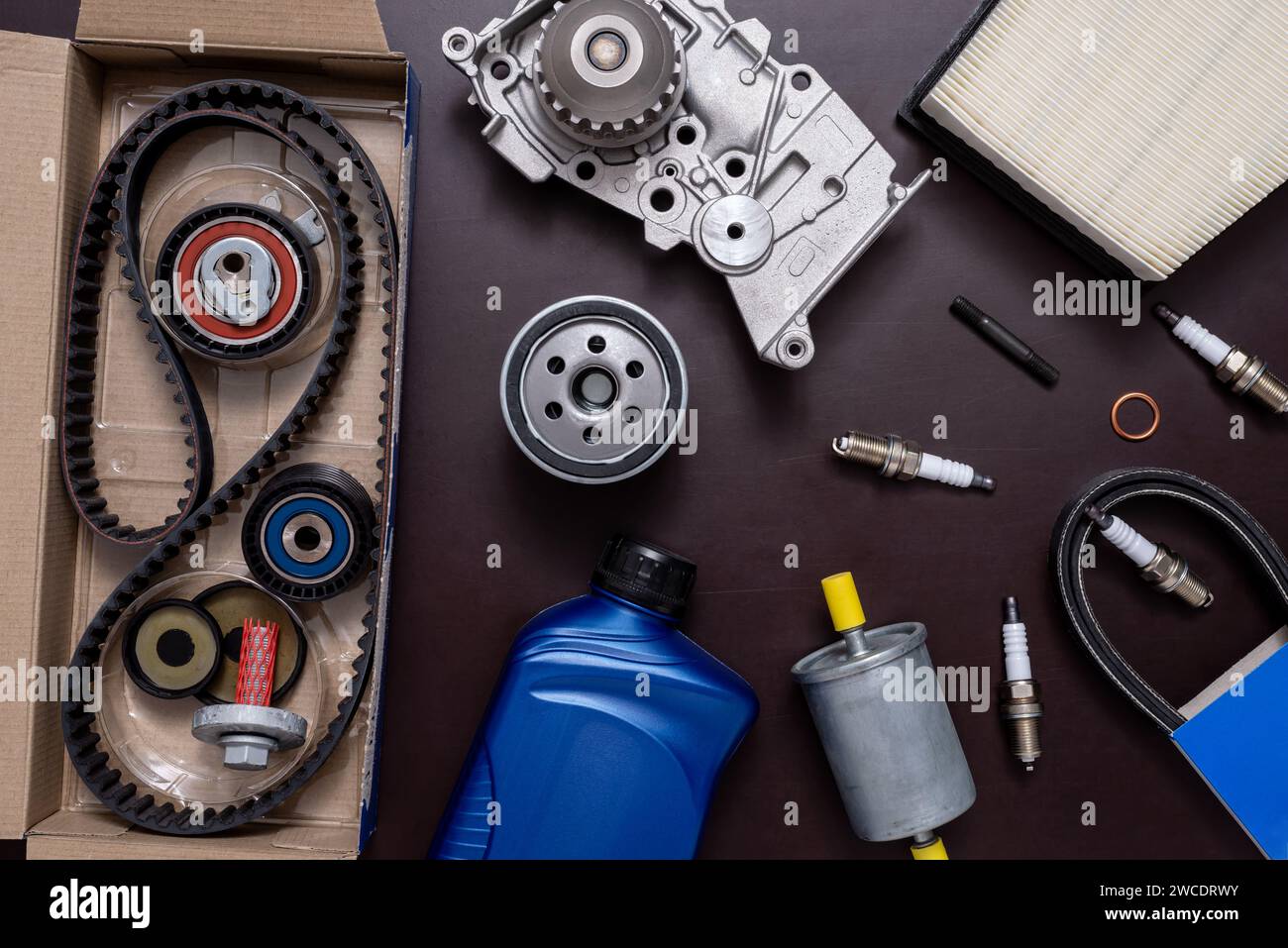 Kit di riparazione per la sostituzione della cinghia di distribuzione in una scatola di cartone aperta e pompa di raffreddamento, candele e filtri su un tavolo di lavoro. Foto Stock