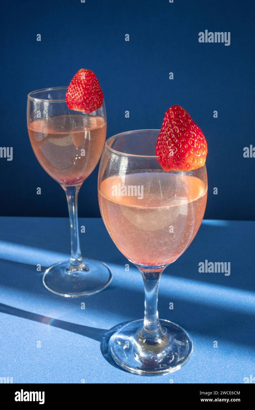Due eleganti bicchieri ripieni di vino rosso sono posti uno accanto all'altro, accompagnati da un piatto di succulente fragole Foto Stock