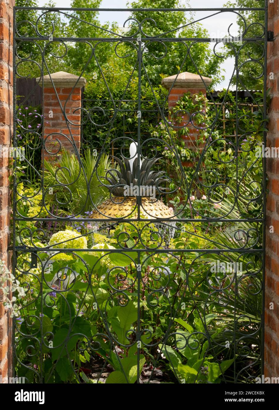 Una vista attraverso un cancello di ferro battuto verso una fontana circondata da una varietà di piante nell'Explore Charleston: Benvenuti al Charleston Garden Foto Stock