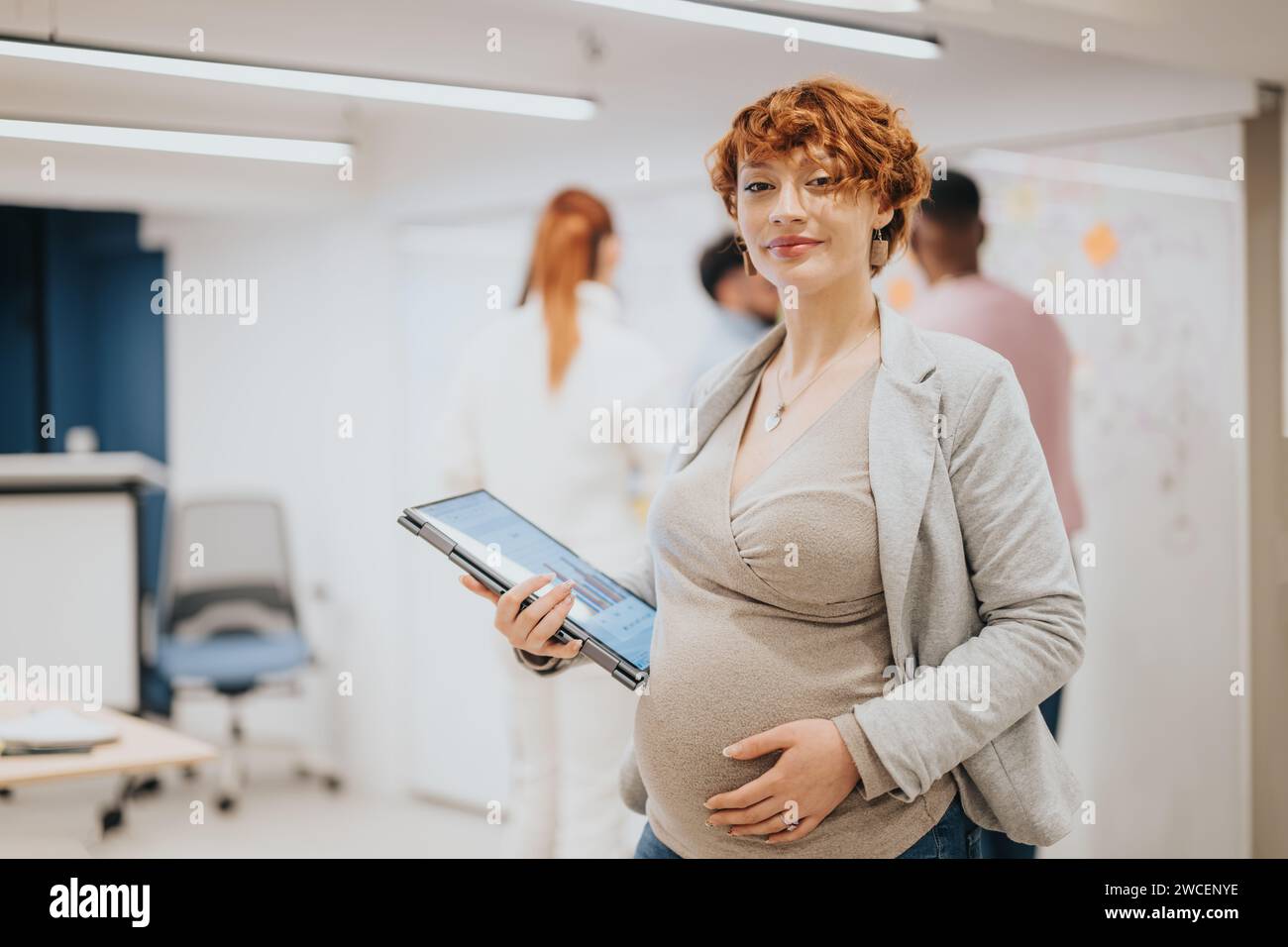 Donna d'affari che tiene in posa un notebook mentre i suoi compagni di squadra collaborano in ufficio. Foto Stock