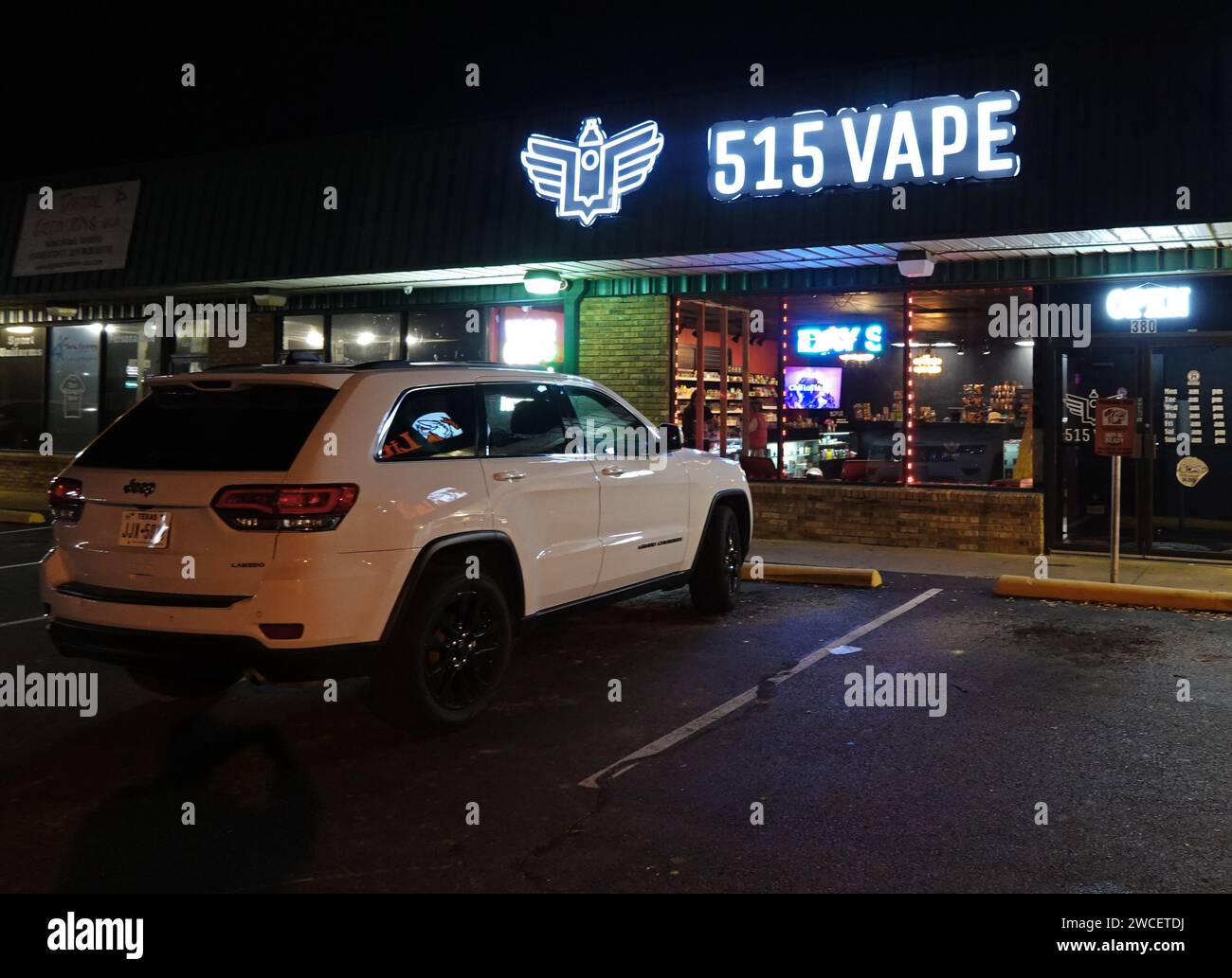 Un SUV bianco parcheggiato di fronte a un negozio di Vape di notte - novembre 2023 Foto Stock