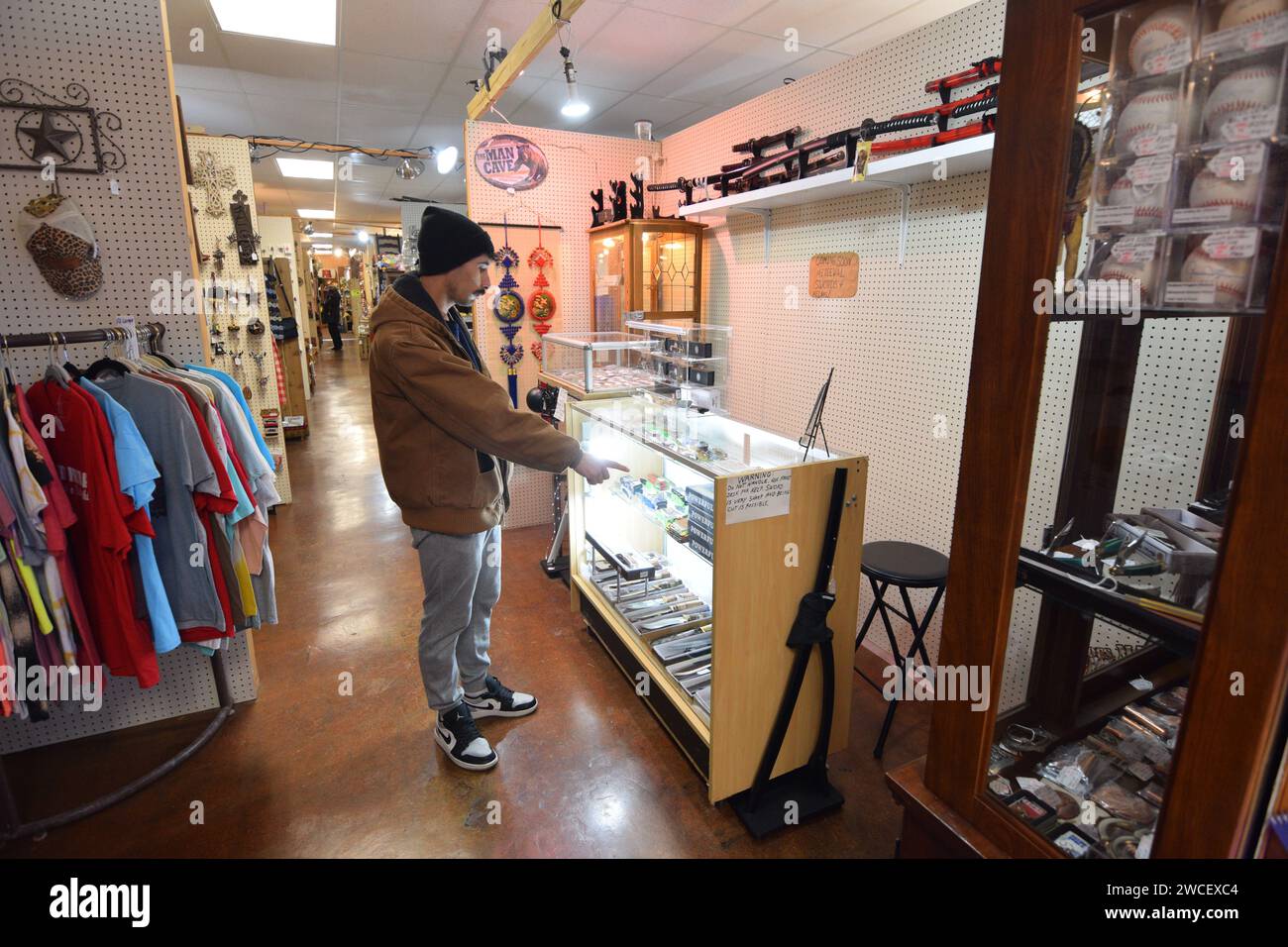 Young Generation Z uomo in cappellino di lana che guarda un'esposizione di coltelli in un negozio di antiquariato - novembre 2023 Foto Stock