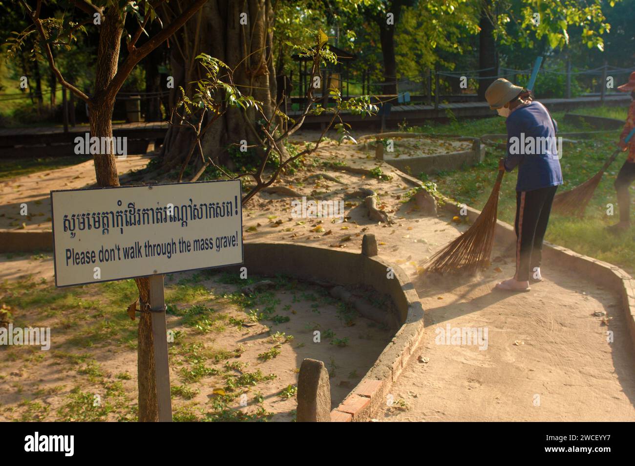 Le signore spazzano le foglie intorno a un albero di uccisione nei campi di sterminio del Choung EK genocidal Center, Phnom Penh, Cambogia. Foto Stock