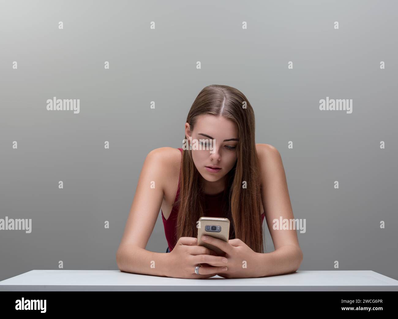 Incastonata nel suo telefono, l'attenzione della donna riflette l'assorbimento dell'era digitale, la parte superiore marrone in contrasto con il grigio Foto Stock