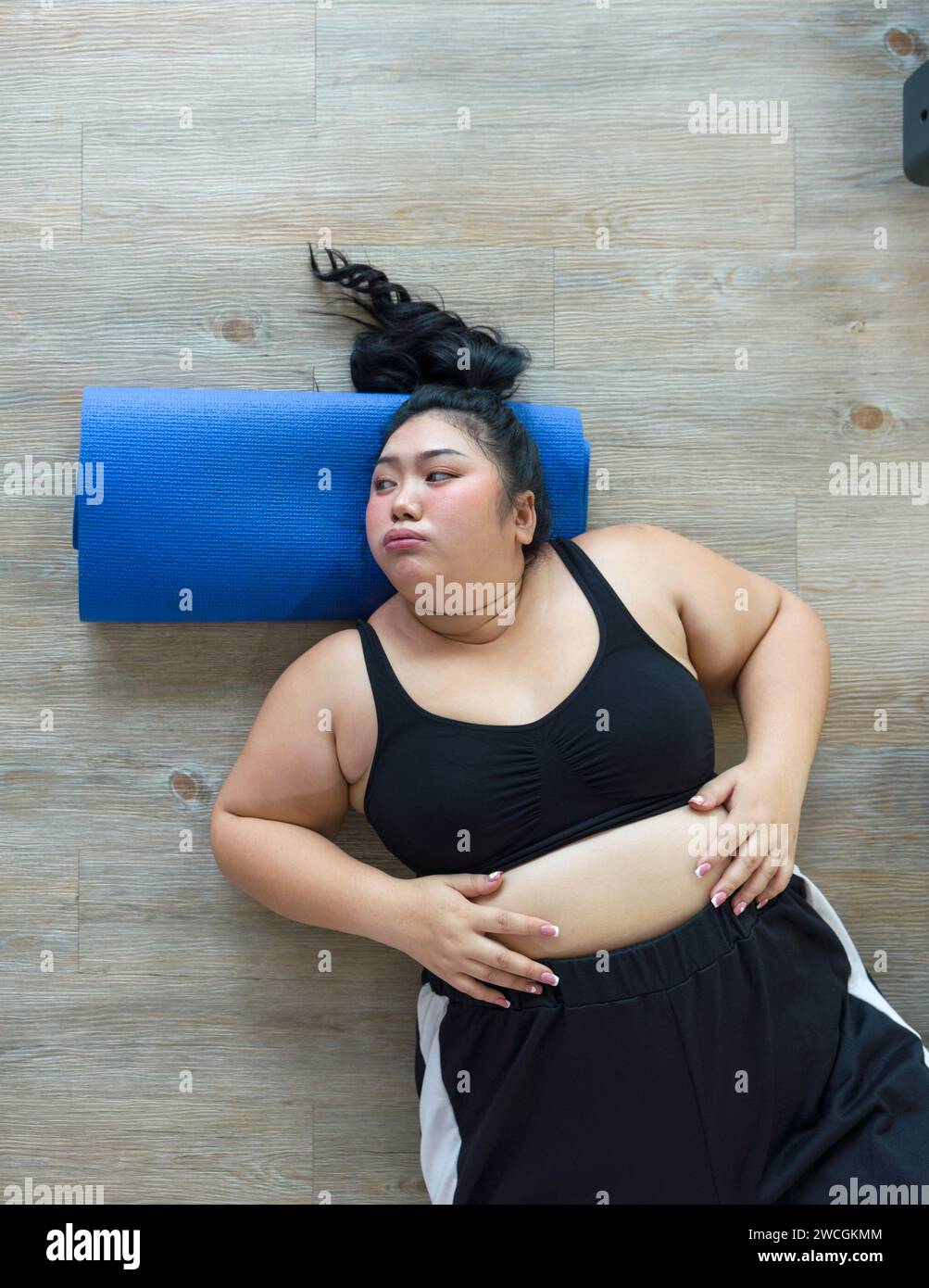 Una donna più grande si stende su un colorato tappetino yoga sul pavimento, rilassandosi dopo una rilassante sessione di yoga in una sala calma. Vista dall'alto Foto Stock
