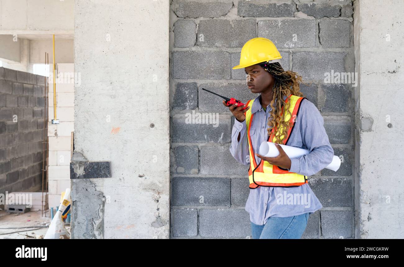 Un costruttore con un casco e un giubbotto luminoso si trova in un cantiere edile. Foto Stock