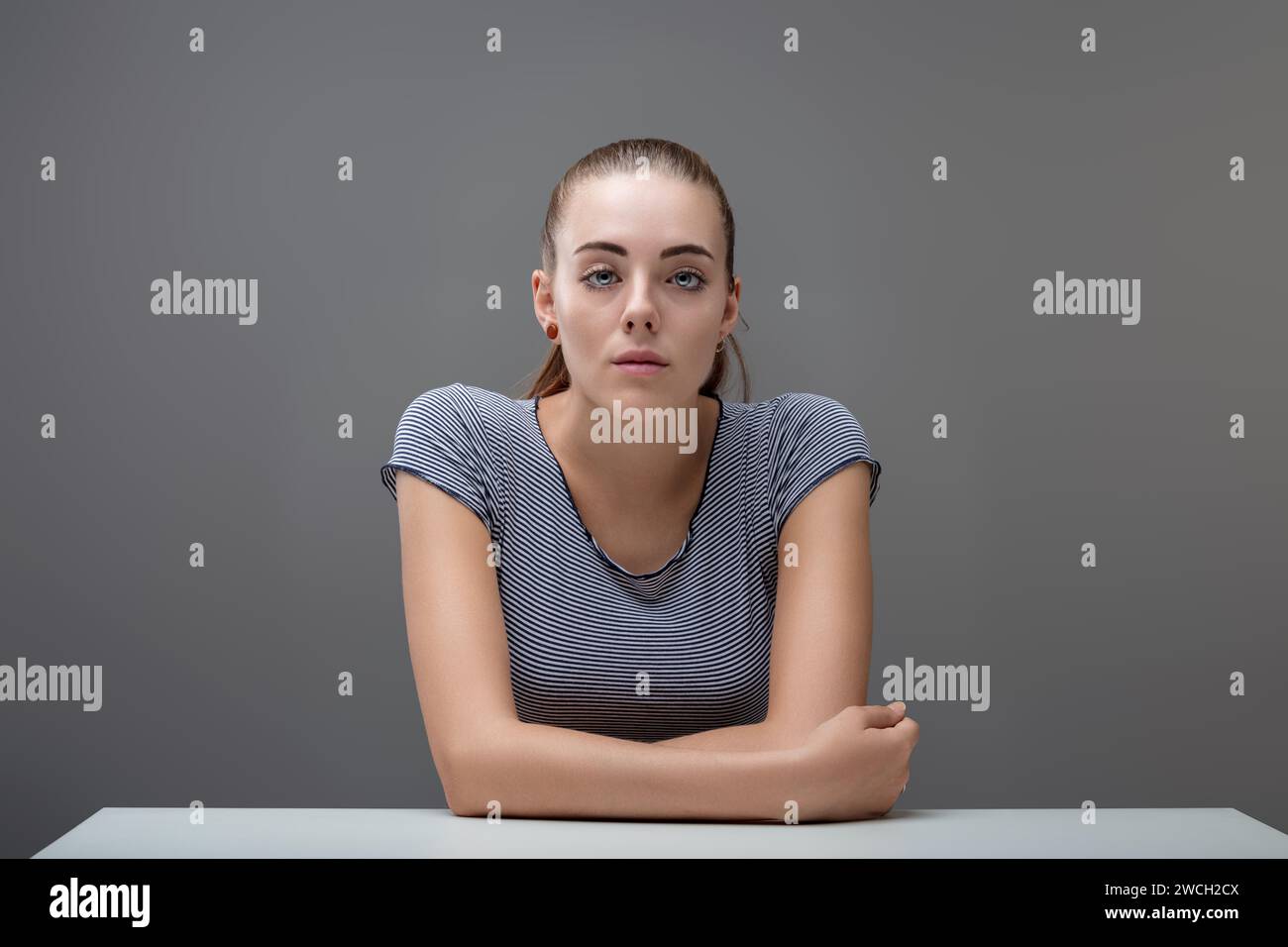 Appoggiandosi con i gomiti sullo scaffale, una bella giovane donna ti guarda senza espressioni e con attenzione. Sapere per deliberare è ciò che lei h Foto Stock