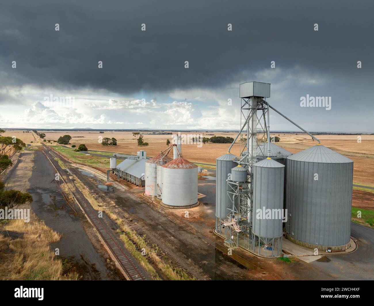 Vista aerea dei silos di grano lungo una linea ferroviaria rurale con nuvole scure e pioggia in lontananza a Moolort nel Victoria centrale, Australia. Foto Stock