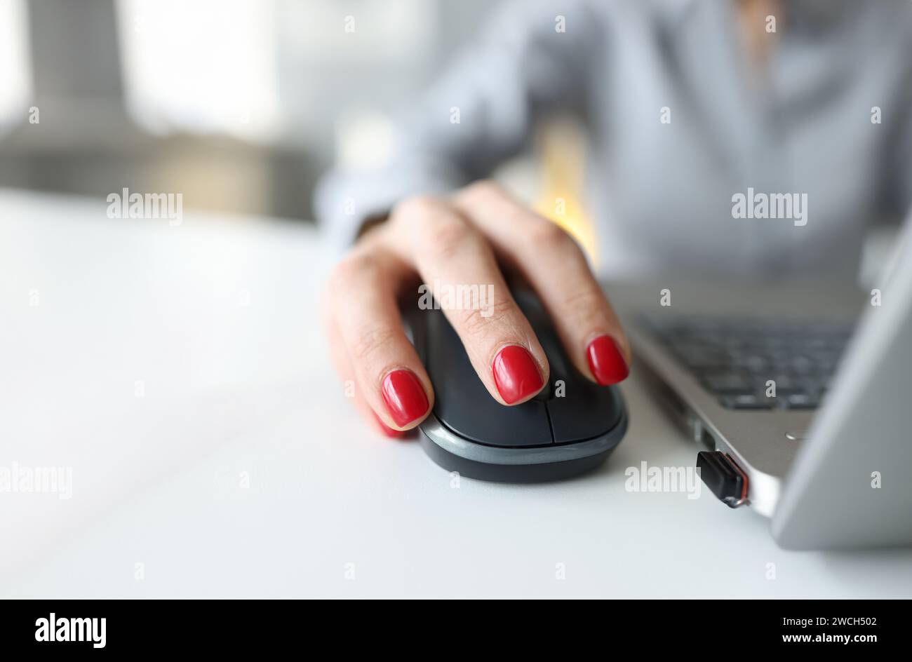 Donna con manicure rosso che tiene il mouse del computer vicino al closeup del laptop Foto Stock